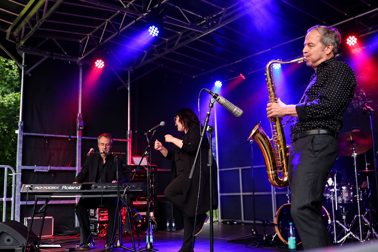 Liveband mit Saxofon, Gesang und Keyboard auf einer beleuchteten Open-Air-Bühne