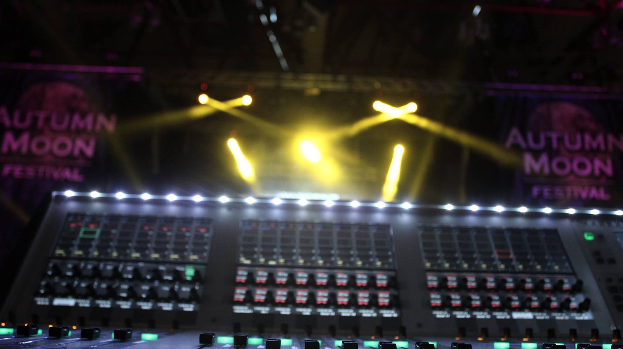 Mischpult vor einer Festivalbühne mit gelben Lichtstrahlen