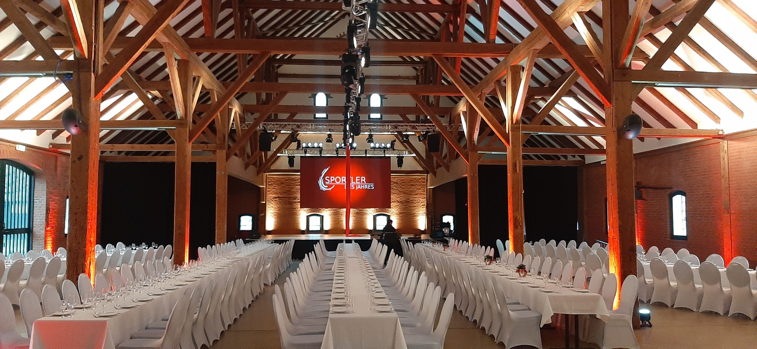 Festlich eingedeckte Halle mit Bühne und warmer Architekturbeleuchtung